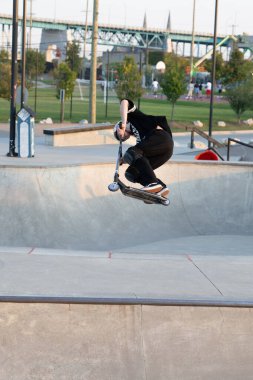 Kaykaycılar ve scooterlar numaralarını güneşli bir yaz gününde halka açık olan açık bir kaykay parkında yapıyorlar.