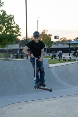 Kaykaycılar ve scooterlar numaralarını güneşli bir yaz gününde halka açık olan açık bir kaykay parkında yapıyorlar.