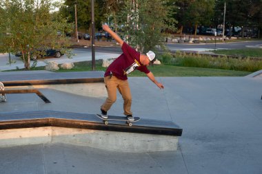 Kaykaycılar ve scooterlar numaralarını güneşli bir yaz gününde halka açık olan açık bir kaykay parkında yapıyorlar.