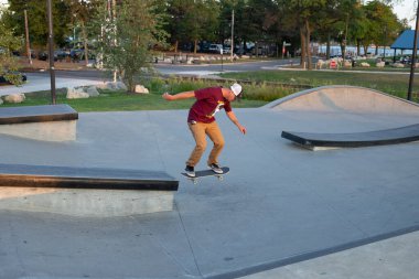 Kaykaycılar ve scooterlar numaralarını güneşli bir yaz gününde halka açık olan açık bir kaykay parkında yapıyorlar.