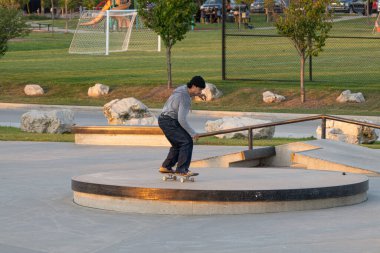 Kaykaycılar ve scooterlar numaralarını güneşli bir yaz gününde halka açık olan açık bir kaykay parkında yapıyorlar.