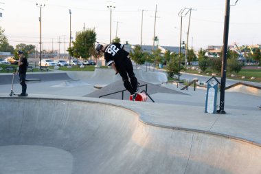 Kaykaycılar ve scooterlar numaralarını güneşli bir yaz gününde halka açık olan açık bir kaykay parkında yapıyorlar.