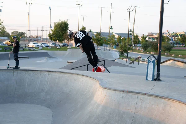 Kaykaycılar ve scooterlar numaralarını güneşli bir yaz gününde halka açık olan açık bir kaykay parkında yapıyorlar.