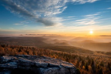 Güzel dağ zirveleri üzerinde dramatik gündoğumu. Çek Milli Parkı. Bulutların ve ormanın üzerinde güneş ışığıyla renkli gökyüzü. Decinsky Sneznik, Çek Cumhuriyeti