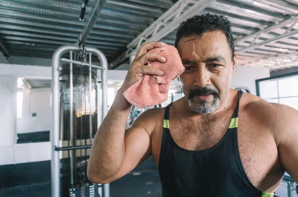 mature man wiping sweat after his exercise routine in the gym