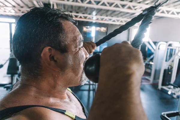 Mature man in sweat performing gym routine, side view, rope cable push m