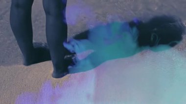 Deniz dalgaları dişilerin bacaklarını yıkar. Mavi hareket eden duman. Çift pozlama efekti