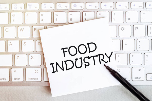 лист бумаги с текстом FOOD INDUSTRY на клавиатуре на белом фоне с черным фломастером
