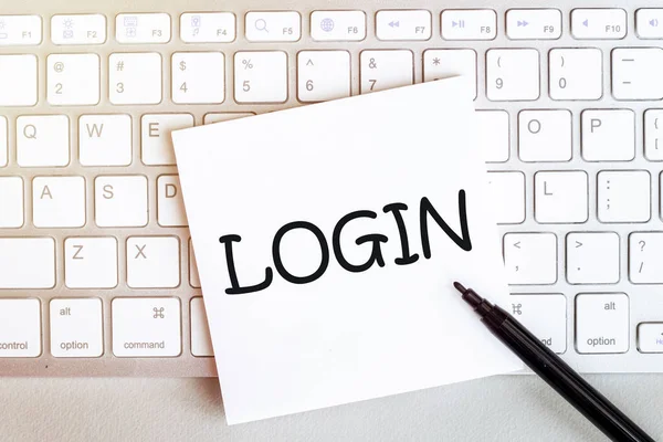 piece of paper with text Login on the keyboard on a white background with a black felt-tip pen