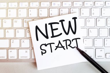 Beyaz arkaplanda siyah keçeli kalemle klavyede yeni bir başlangıç metni olan kağıt parçası