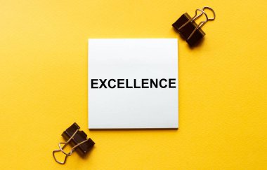 Kırtasiyeli sarı arkaplan üzerinde EXCELLENCE metni olan beyaz kağıt