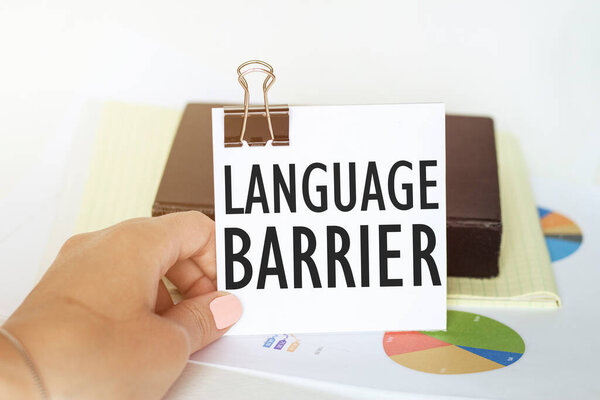 рука женщины держит листок бумаги с текстом LANGUAGE BARRIER на фоне графиков и блокнота
