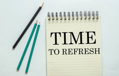 Beyaz arkaplandaki defteri yenilemek için metin zamanı olan iki yeşil bir siyah kalem.