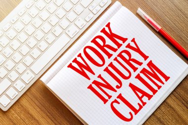 beyaz bir defter üzerinde yazı çalışması INJURY CLAIM bir ahşap yüzey üzerinde yatar kırmızı bir işaret ile beyaz bir klavye