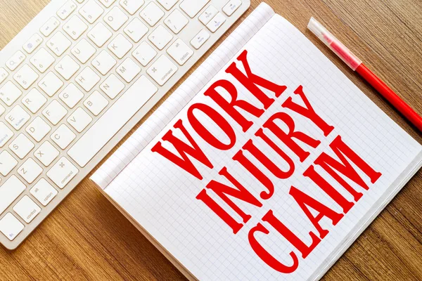 beyaz bir defter üzerinde yazı çalışması INJURY CLAIM bir ahşap yüzey üzerinde yatar kırmızı bir işaret ile beyaz bir klavye