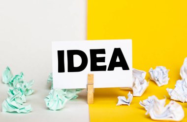 Sarı ve beyaz arkaplanlarda farklı renklerde kağıt desteleri olan bir mandalın üzerinde IDEA metni olan beyaz kağıt