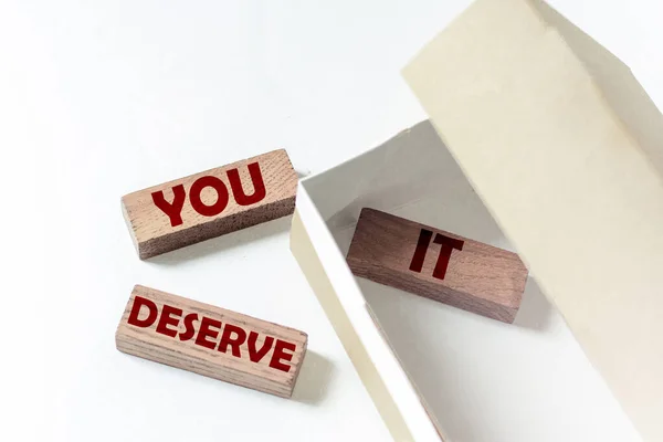 wooden blocks with text You Deserve It in a box on a white background