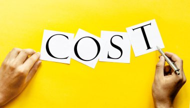 Sarı arkaplanda insan eli ile COST yazılı beyaz kağıt