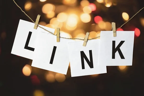 LINK yazılı beyaz kağıt parçaları çok renkli bir bokeh arka planına karşı bir ipe asılıyor