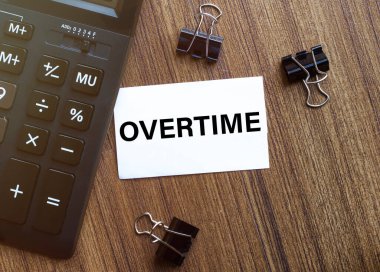 Kırtasiyeli siyah arkaplan üzerinde fazla mesai mesajı olan beyaz kağıt