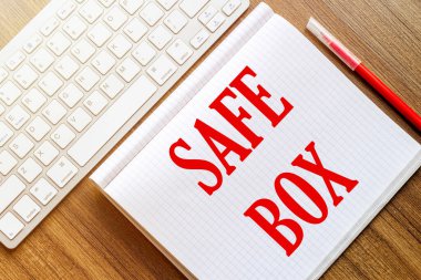 Metin Kutusu olan beyaz bir defter kırmızı işaretli beyaz bir klavyenin yanındaki ahşap bir yüzeyde duruyor.