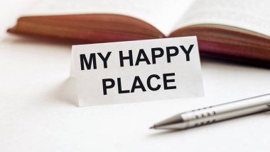 Beyaz arka planda, kitapların, kalemlerin ve mutlu yerimin yazılı olduğu bir kağıt parçası.