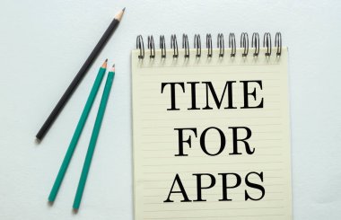 Beyaz arkaplandaki defterdeki uygulamalar için metin zamanı olan iki yeşil bir siyah kalem.