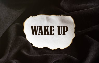 Yazılı yanmış beyaz kağıt parçası. Siyah kumaş arka planda uyan.