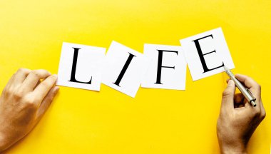 Yazılı beyaz kağıt. Sarı arka planda insan eli ile hayat.