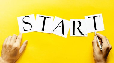 Yazılı beyaz kağıt. Sarı arkaplanda insan eliyle başla.