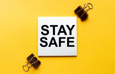 Yazılı beyaz kağıt. Kırtasiyeli sarı arkaplanda güvende ol.