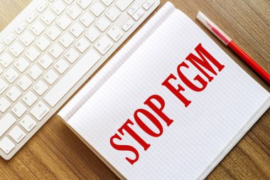 Metni olan beyaz bir defter. Stop Fgm kırmızı işaretli beyaz bir klavyenin yanındaki ahşap bir yüzeyde yatıyor.