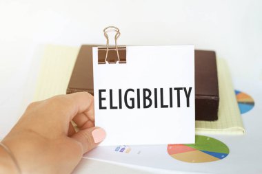 Kadın eli, arkaplanda grafikler ve not defterleri olan bir kağıt parçası tutuyor.