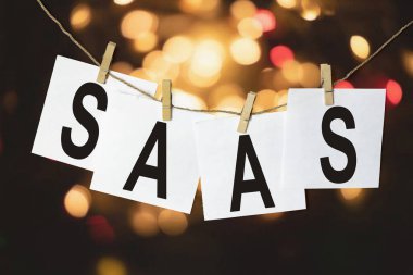 Hizmet olarak SaaS yazılımına sahip beyaz kağıt parçaları çok renkli bir bokeh arka planına karşı bir ipe tutunur