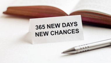 Beyaz arkaplan üzerinde kitap, kalem ve kalemlerin arka planında 365 Yeni Gün yazılı bir kağıt parçası