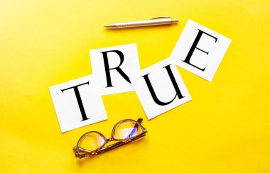 Yazılı beyaz kağıt. Sarı zemin üzerinde gözlük ve kalemle gerçek.