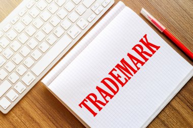 Metin markalı beyaz bir defter kırmızı işaretli beyaz bir klavyenin yanındaki ahşap bir yüzeyde duruyor.