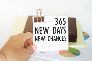 Kadının elinde, üzerinde 365 Yeni Gün yazan bir kağıt parçası var. Grafikler ve not defterlerinin arka planında Yeni Şanslar