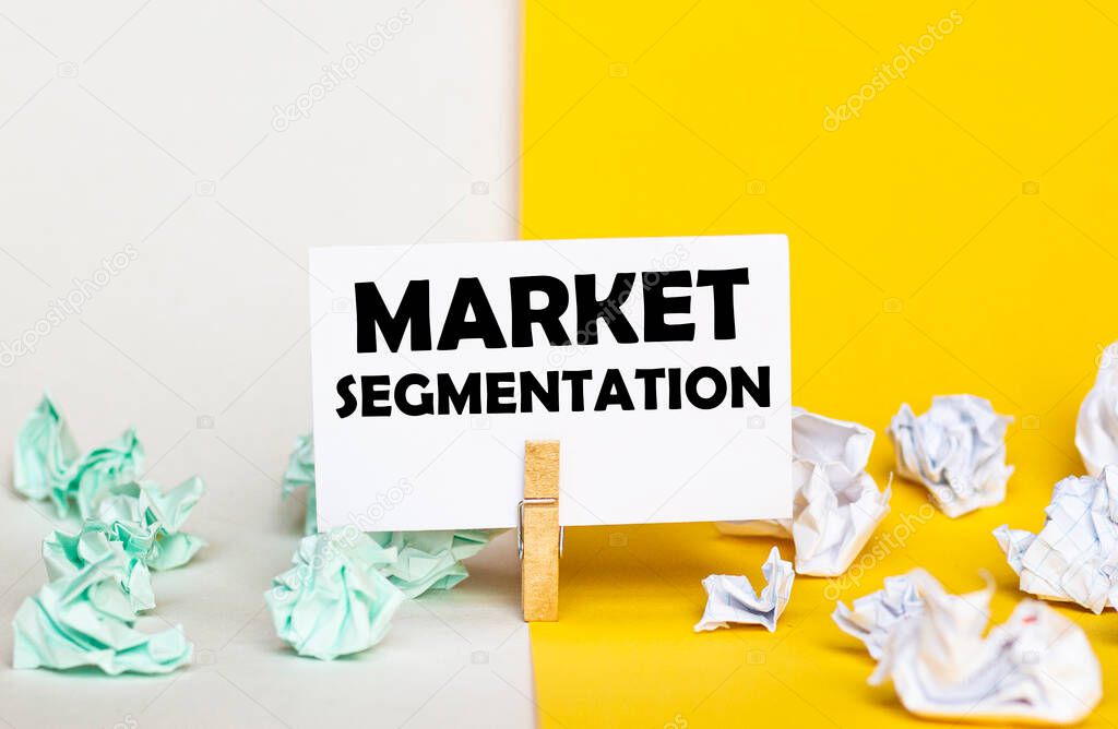 white paper with text Market Segmentation on a clothespin on yellow and white backgrounds with paper wads of different colors