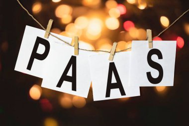 Hizmet olarak PaaS Platformu metni olan beyaz kağıt parçaları çok renkli bir bokeh arka planına karşı bir ipe tutunur