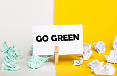 Sarı ve beyaz arkaplanlarda farklı renklerde kağıt desteleri olan çamaşır mandalına yazı yazan beyaz kağıt Go Green