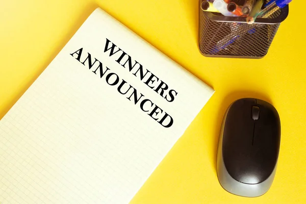 computer mouse, pens, felt-tip pens, notepad with text Winners Announced on a yellow background