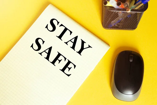 computer mouse, pens, felt-tip pens, notepad with text Stay Safe on a yellow background