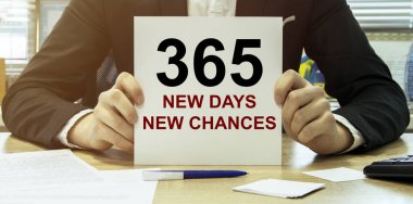 Adam, ofis geçmişi olan gömlekte 365 Yeni Gün yazılı bir kağıt al.