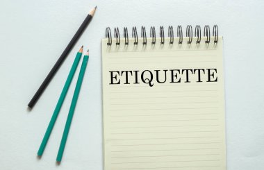Beyaz arkaplandaki defterde ETIQUETTE yazılı iki yeşil bir siyah kalem
