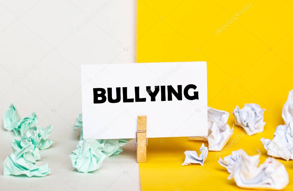 white paper with text Bullying on a clothespin on yellow and white backgrounds with paper wads of different colors