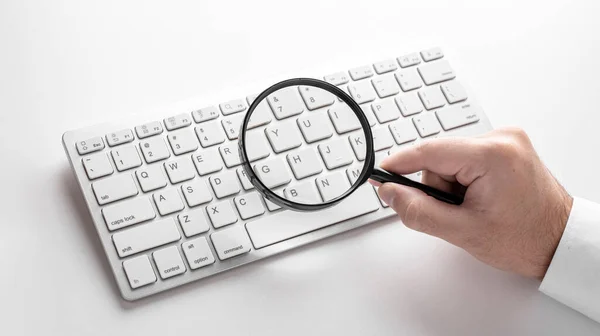 black magnifier on a white keyboard on a white background. Business concept.