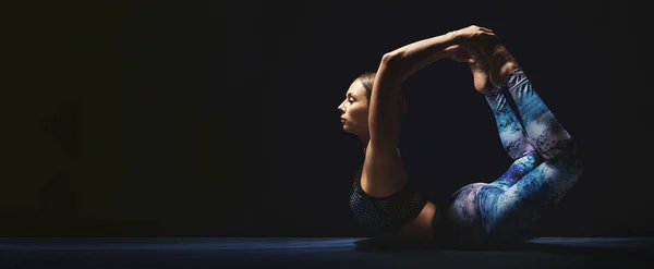 Sportowa młoda kobieta ćwicząca jogę. Czarne tło, urocze światło, pogodny nastrój. — Zdjęcie stockowe