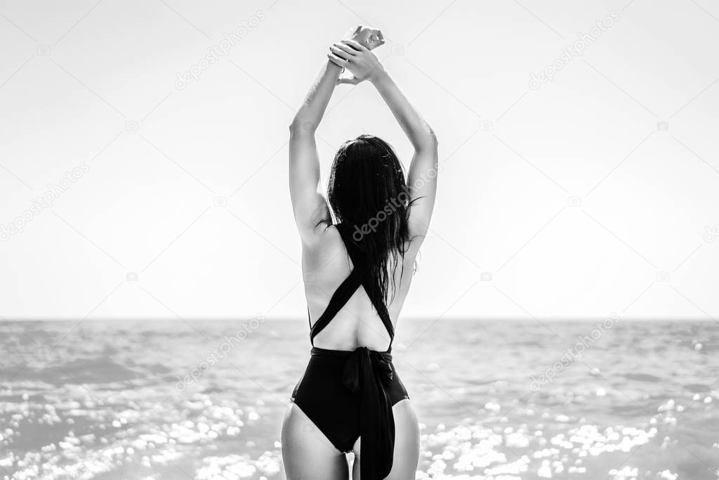 Back view of girl in black swimsuit with sea on backgroun