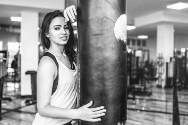 Siyah ve beyaz fotoğraf sportif kız spor salonunda boks torbası sarılma.
